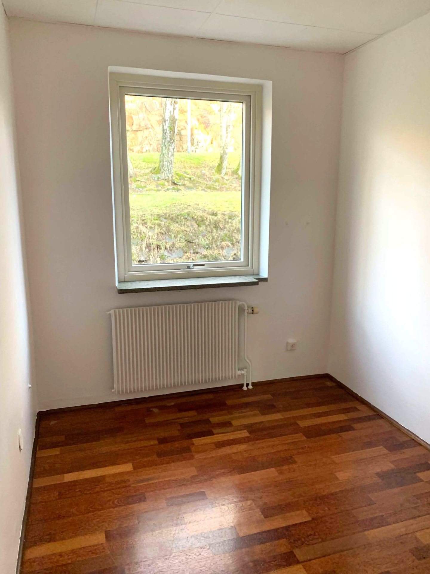 Sovrum med fönster mot grönska och parkettgolv